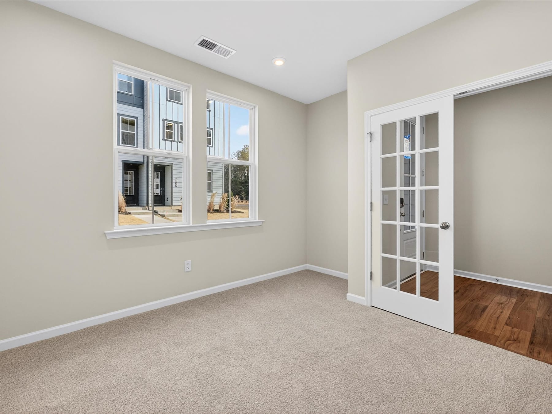 A spacious and well-lit room with a large window, hardwood floors, and a white French door leading to another area.