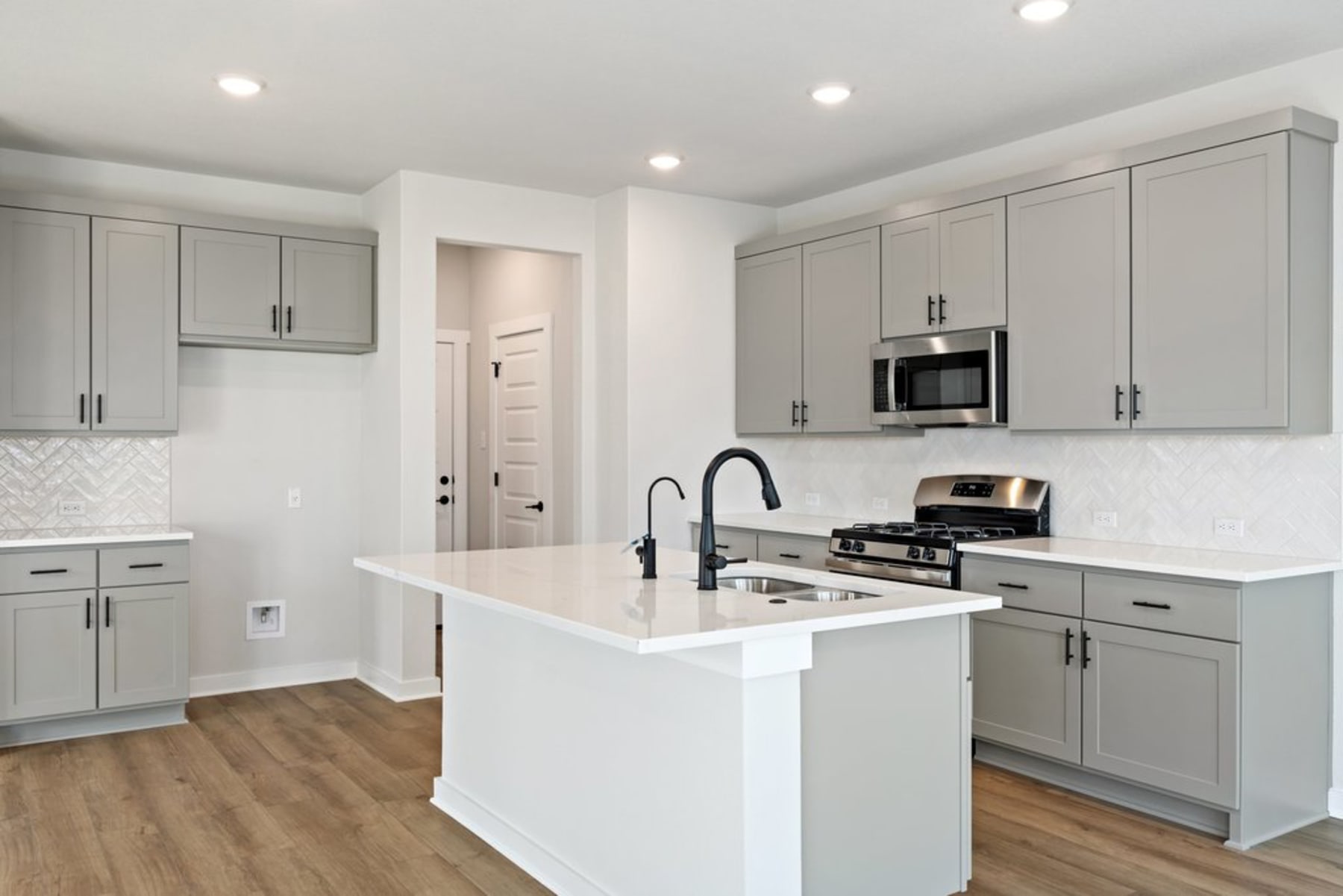 A modern, well-lit kitchen with gray cabinets, a white countertop, and a stainless steel appliance on the island.