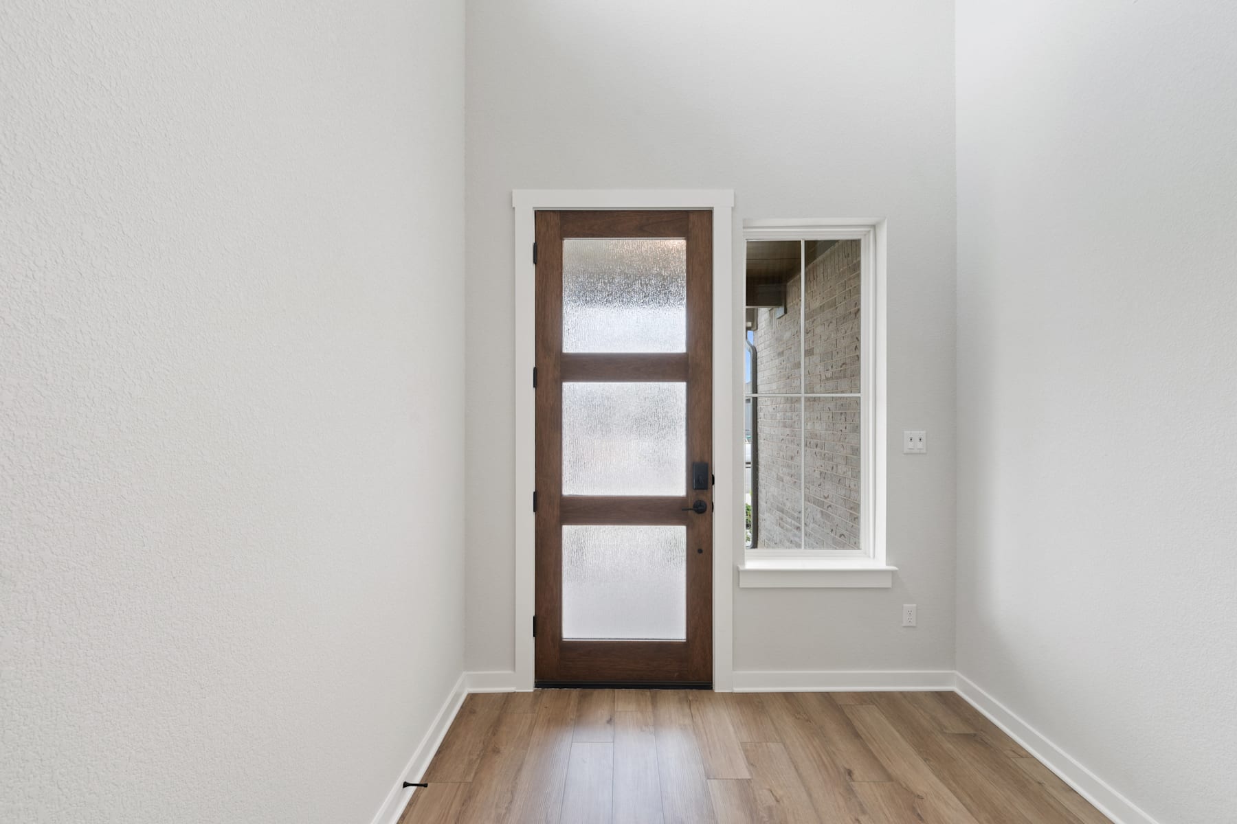 A wooden door with glass panels stands in a corner of a room, with a small window visible in the background.