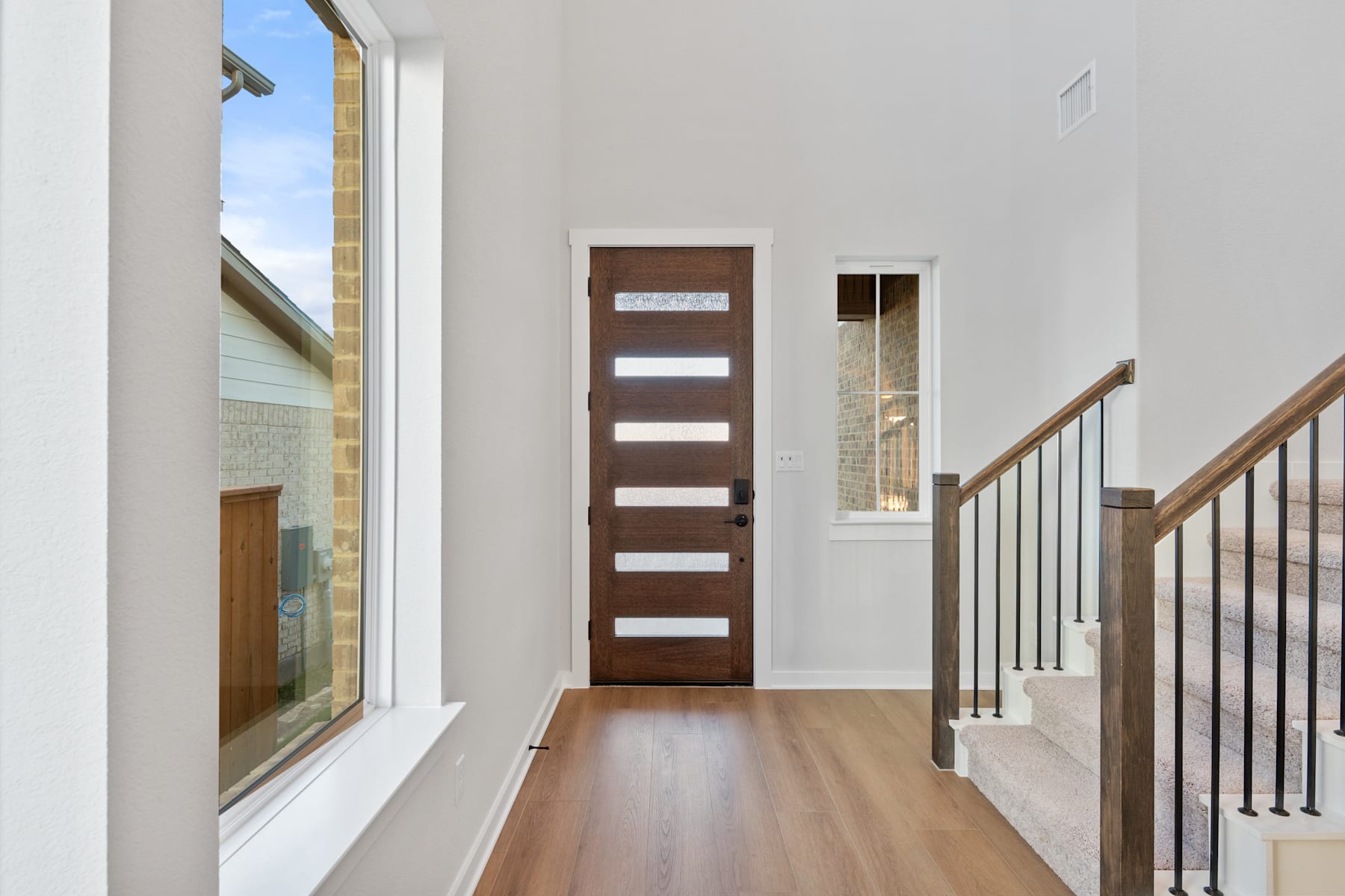 A modern and minimalist entryway with a wooden door, hardwood floors, and a staircase leading to the upper level.