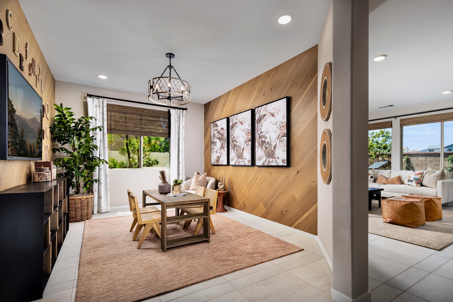 A cozy and inviting dining area with wooden paneled walls, a rustic chandelier, and a wooden table set with chairs, complemented by artwork and potted plants in the background.