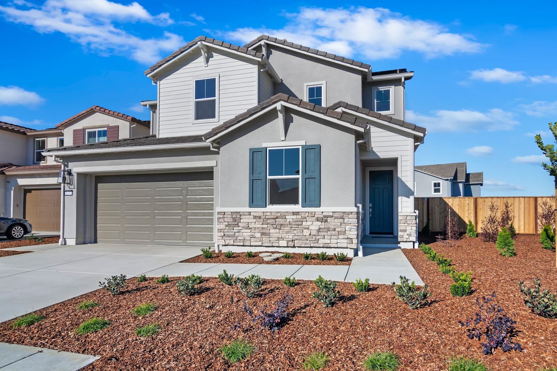 A modern two-story house with a garage, surrounded by a landscaped yard with plants and a clear blue sky in the background.