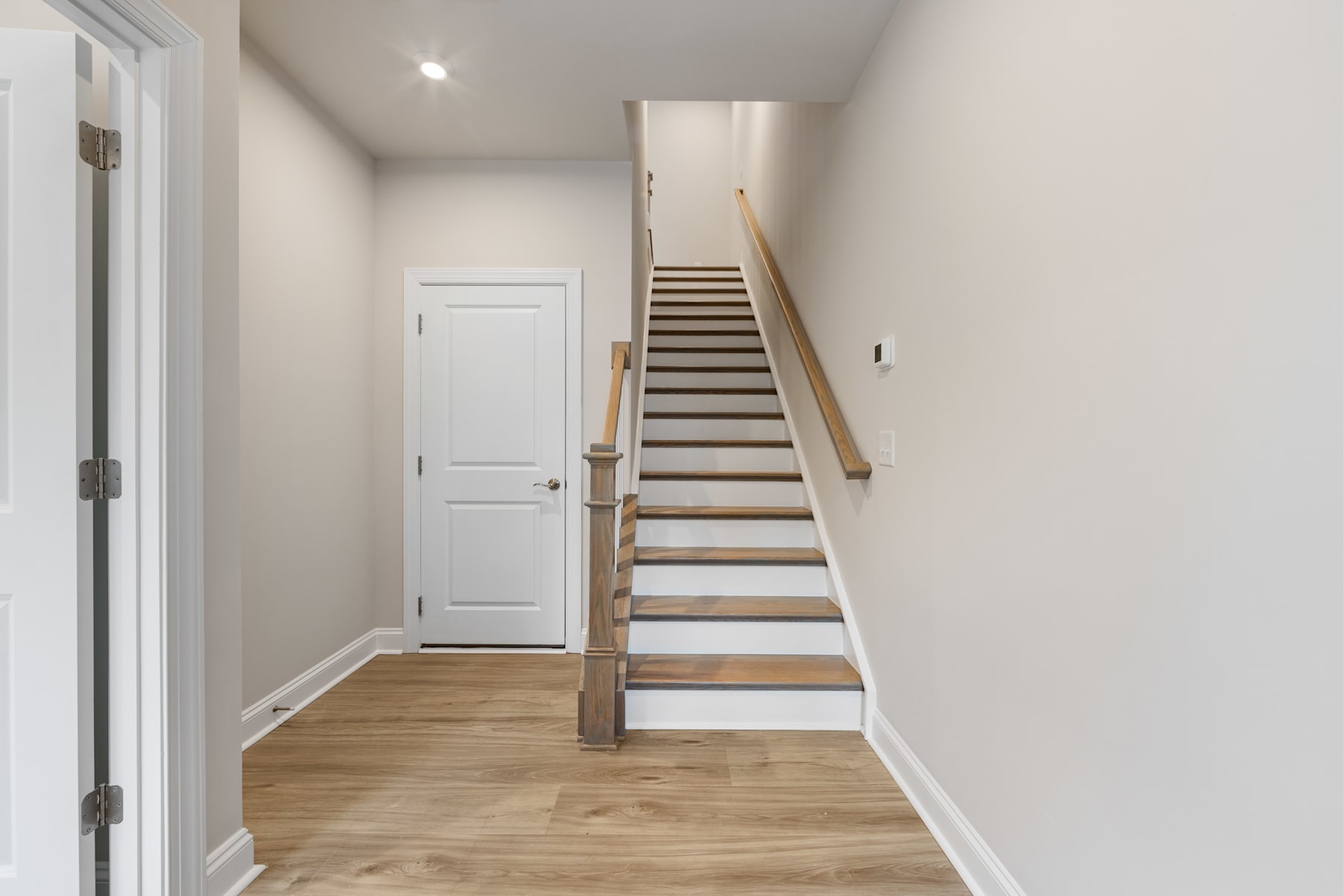 A bright and spacious hallway with a wooden staircase leading upstairs, and a white door visible in the background.