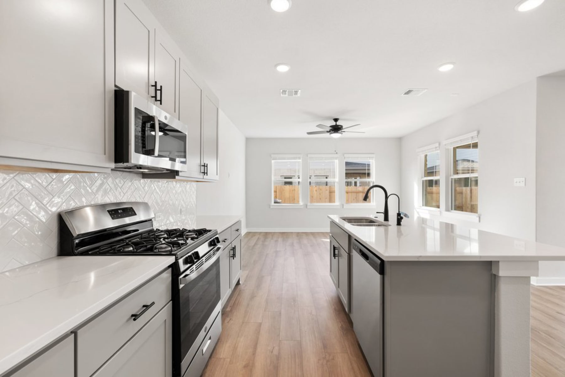 A modern, open-concept kitchen with stainless steel appliances, white cabinets, and a central island with a quartz countertop, set against a bright, airy backdrop with hardwood floors and recessed lighting.