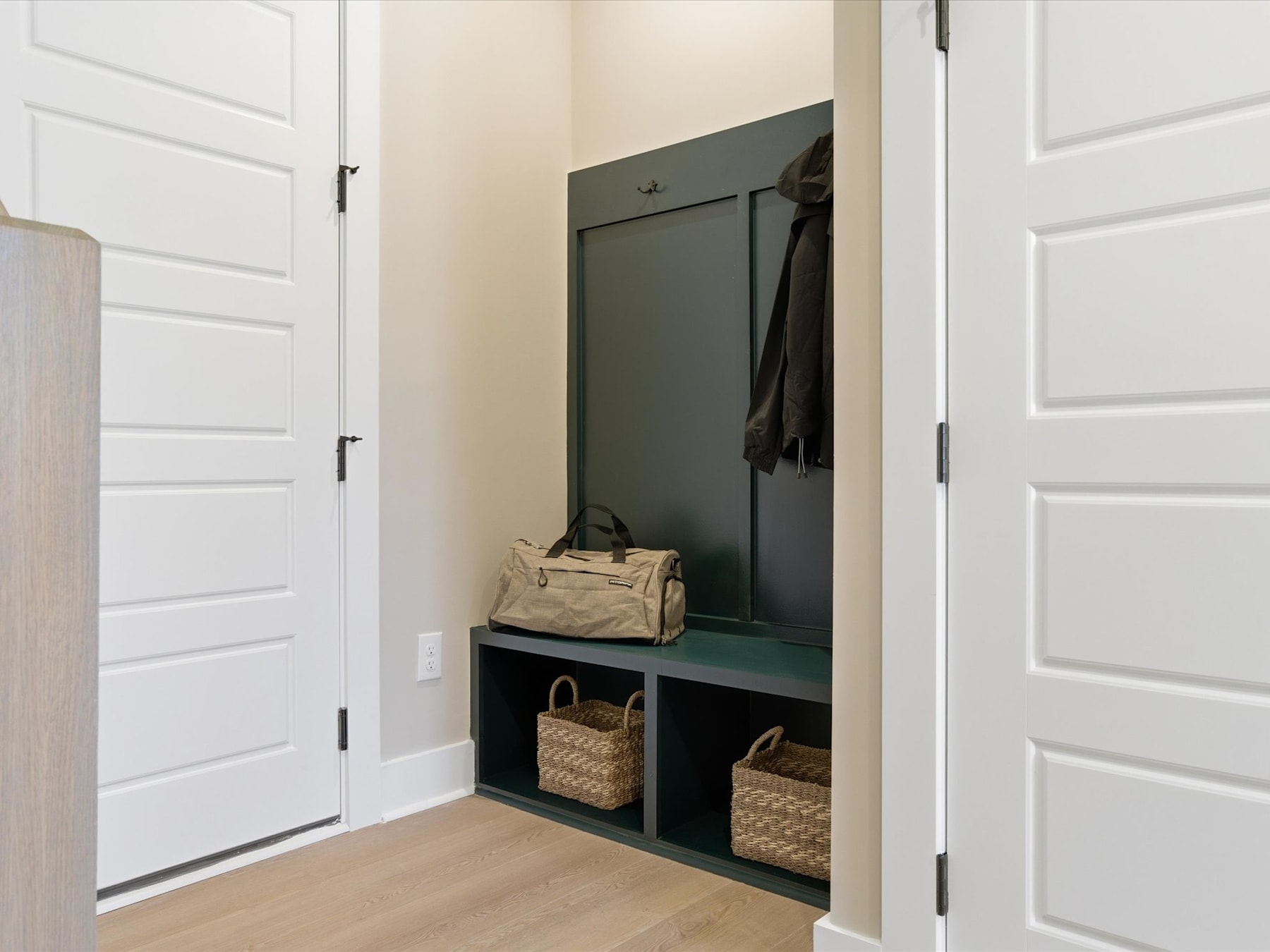 A small entryway with white doors, a green built-in storage unit, and various baskets and bags on the shelves.