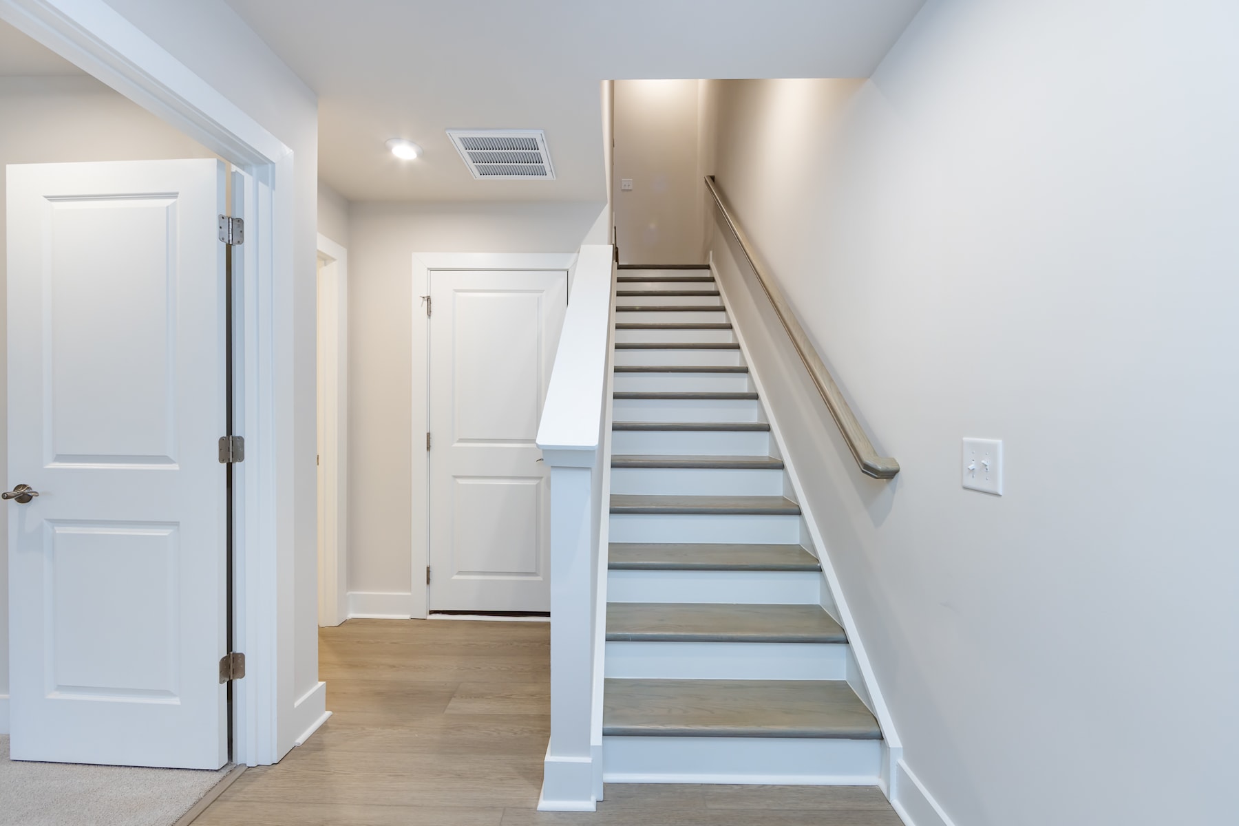 A bright and airy interior with a staircase leading up to the second floor, surrounded by white walls and wooden floors.