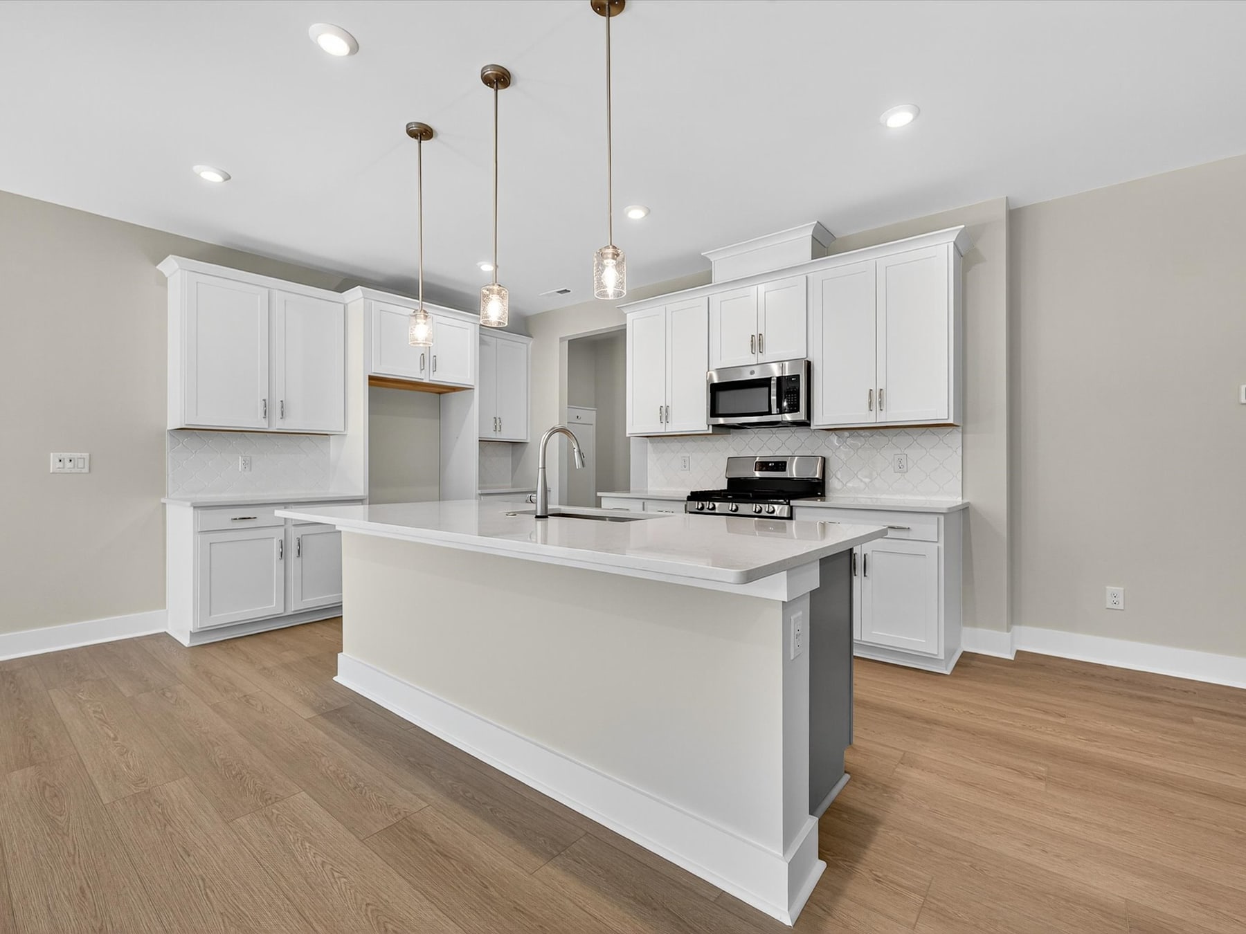 A modern, open-concept kitchen with white cabinets, a central island, and hardwood floors, illuminated by pendant lights.