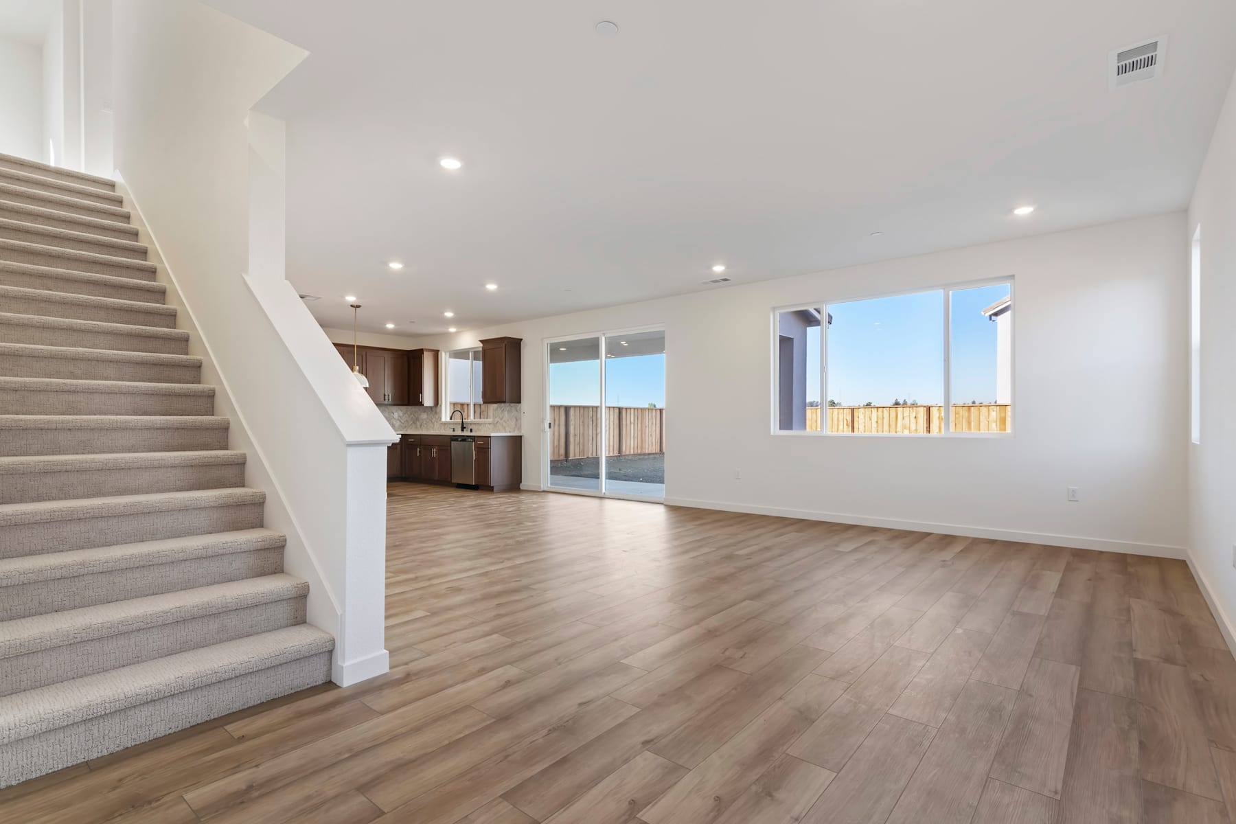 A spacious, open-concept living area with a staircase leading to an upper level, hardwood flooring, and large windows providing ample natural light.