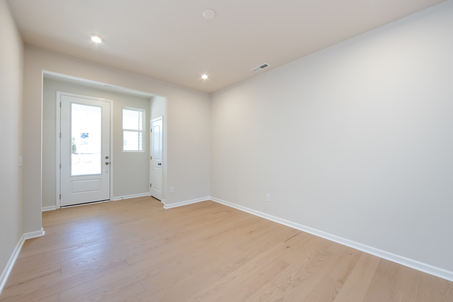 A bright and spacious room with a white wall, a wooden floor, and a glass-paneled door leading to the exterior.