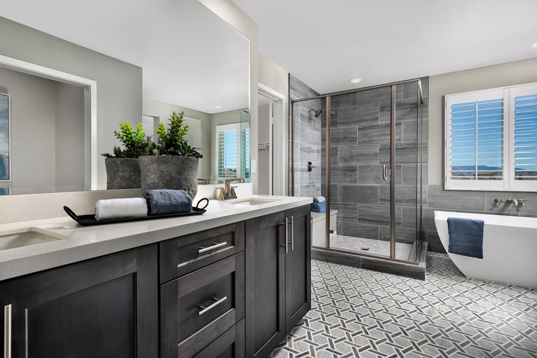 A modern and stylish bathroom with a dark vanity, a large shower enclosure, and a tiled floor featuring a geometric pattern.