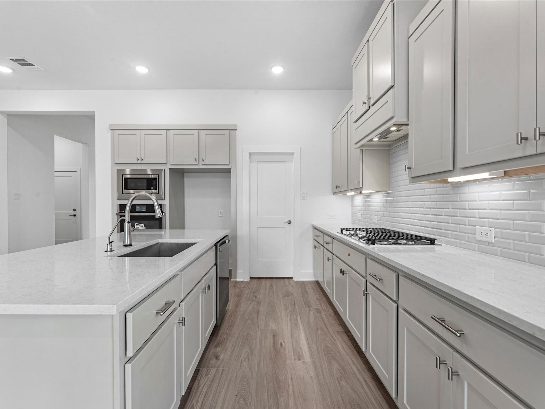 A modern, well-lit kitchen with white cabinets, a tile backsplash, and a wooden floor extends into the background.