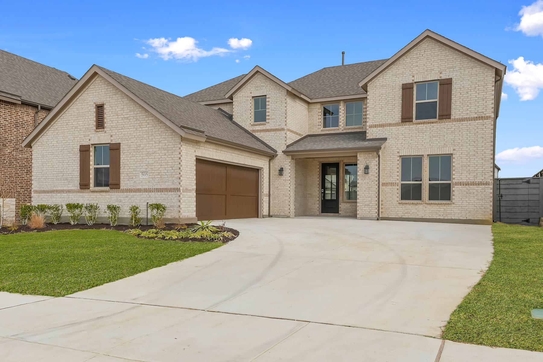 A two-story brick and stone house with a garage, surrounded by a well-manicured lawn and a clear blue sky with scattered clouds in the background.