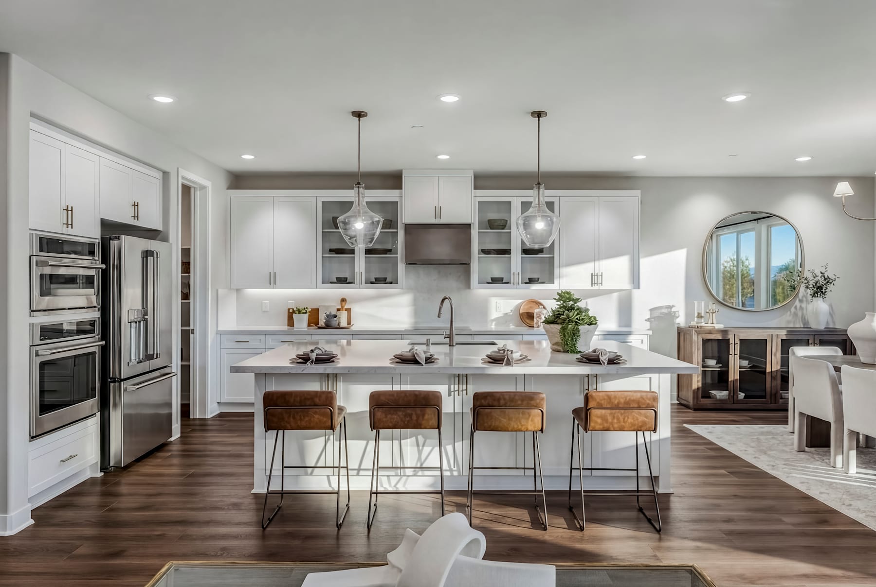 A modern, open-concept kitchen with white cabinets, stainless steel appliances, and a large island with bar stools, set against a backdrop of hardwood floors and a cozy living area.