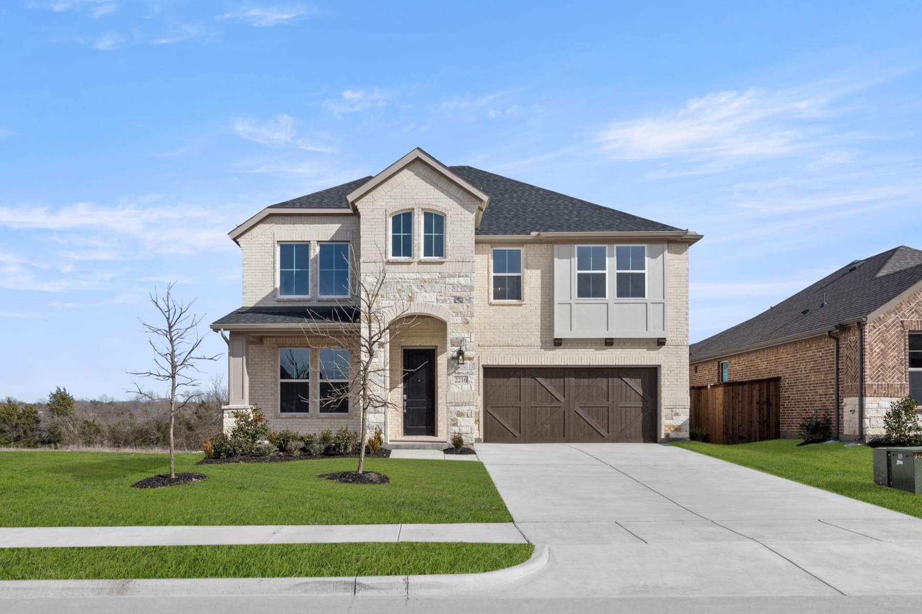 A two-story house with a stone exterior, a garage, and a well-manicured lawn set against a blue sky with scattered clouds.