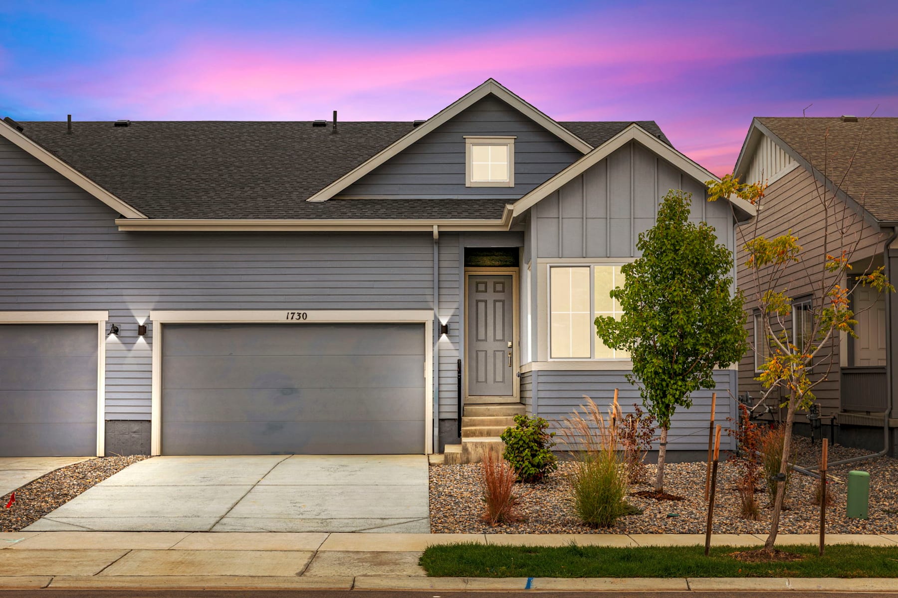 A two-story residential house with a garage, surrounded by landscaping and a vibrant sunset sky in the background.