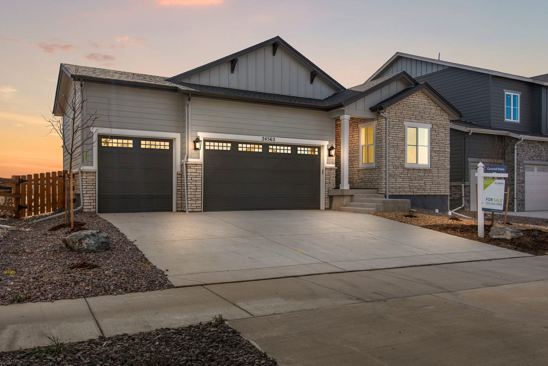 A modern two-story house with a garage and a concrete driveway, set against a backdrop of a cloudy sky at sunset.