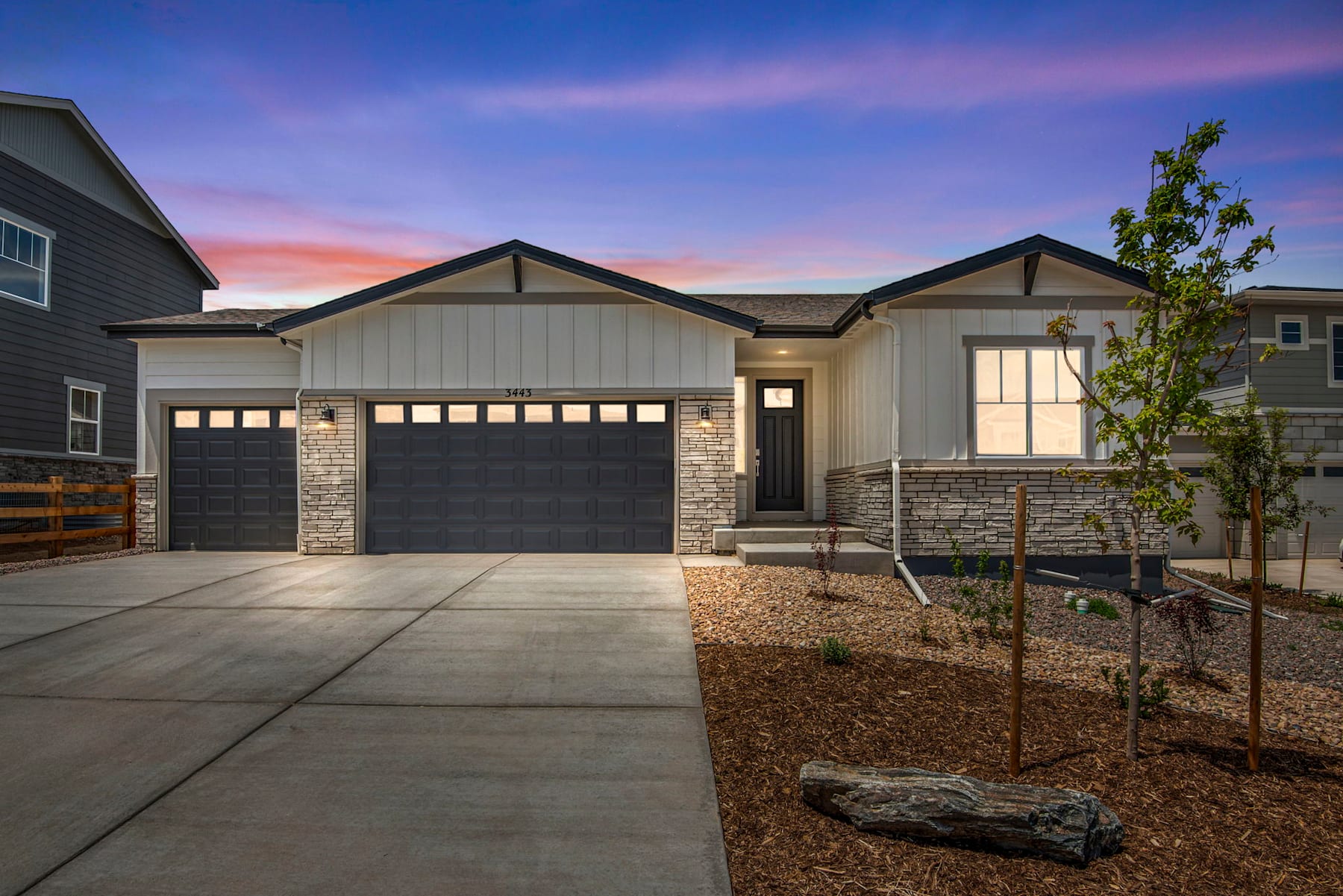 A modern, two-story house with a garage, surrounded by a landscaped yard and a colorful sunset sky in the background.