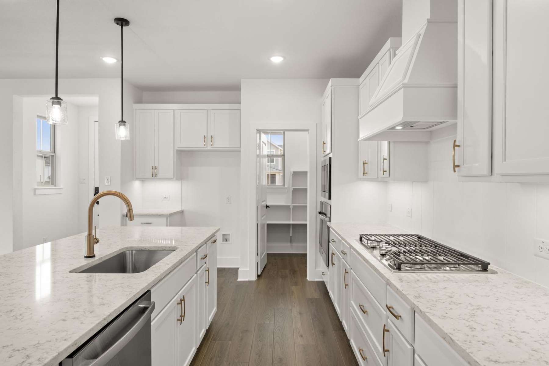 A modern, bright, and spacious kitchen with white cabinets, granite countertops, and hardwood floors, featuring a gas stove and pendant lighting.