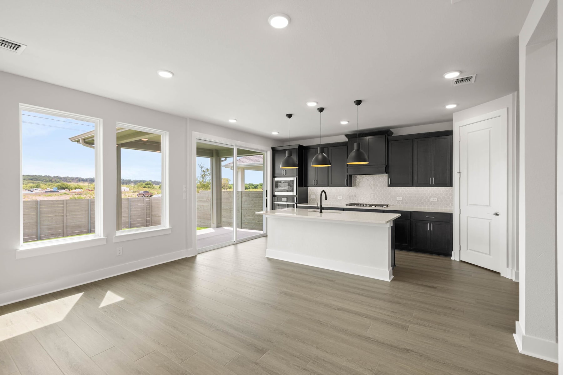 A modern, open-concept kitchen and living space with large windows, dark cabinets, and a white island countertop.