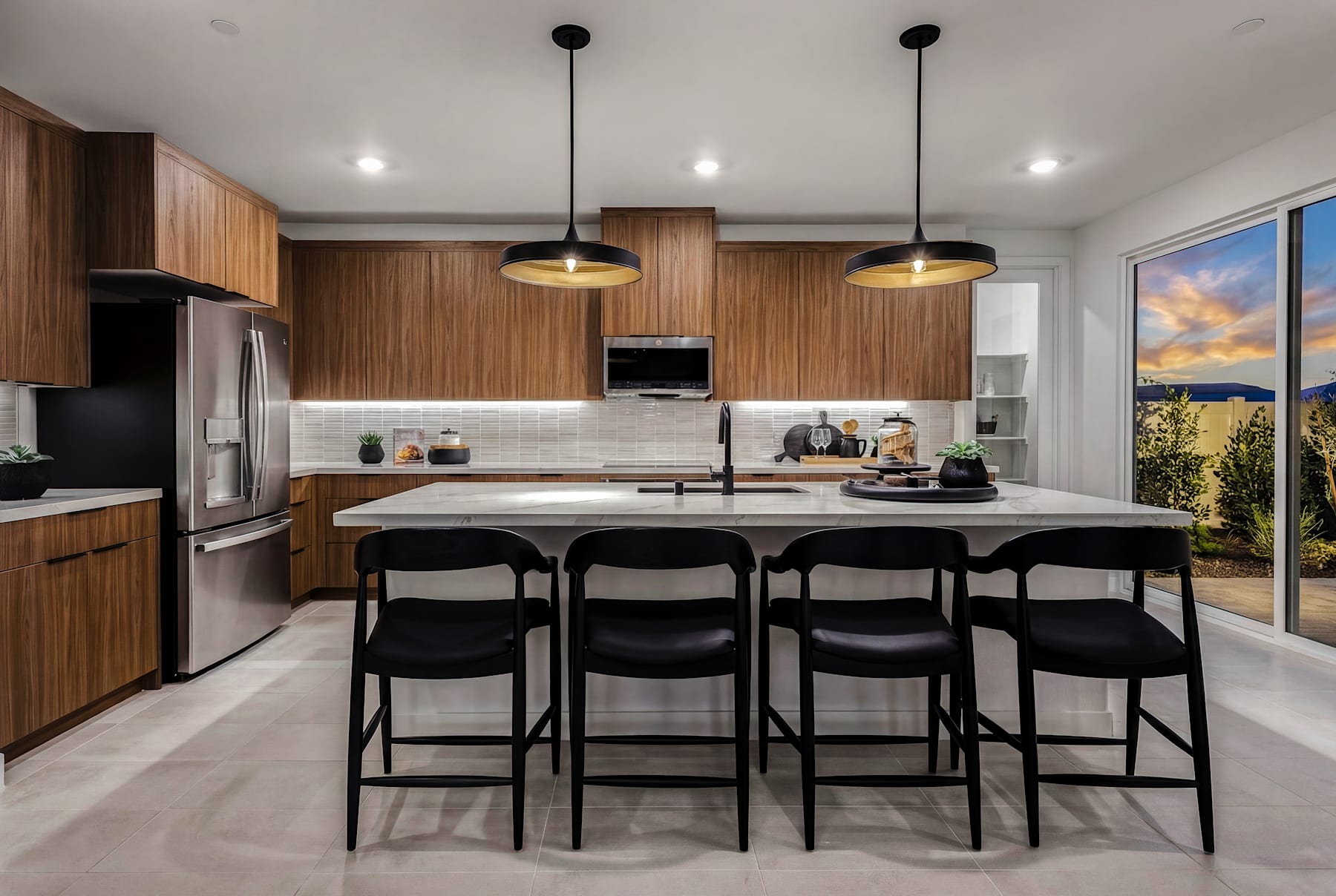 A modern and stylish kitchen with wooden cabinetry, black pendant lights, and a large island with bar stools, set against a backdrop of a scenic outdoor view.