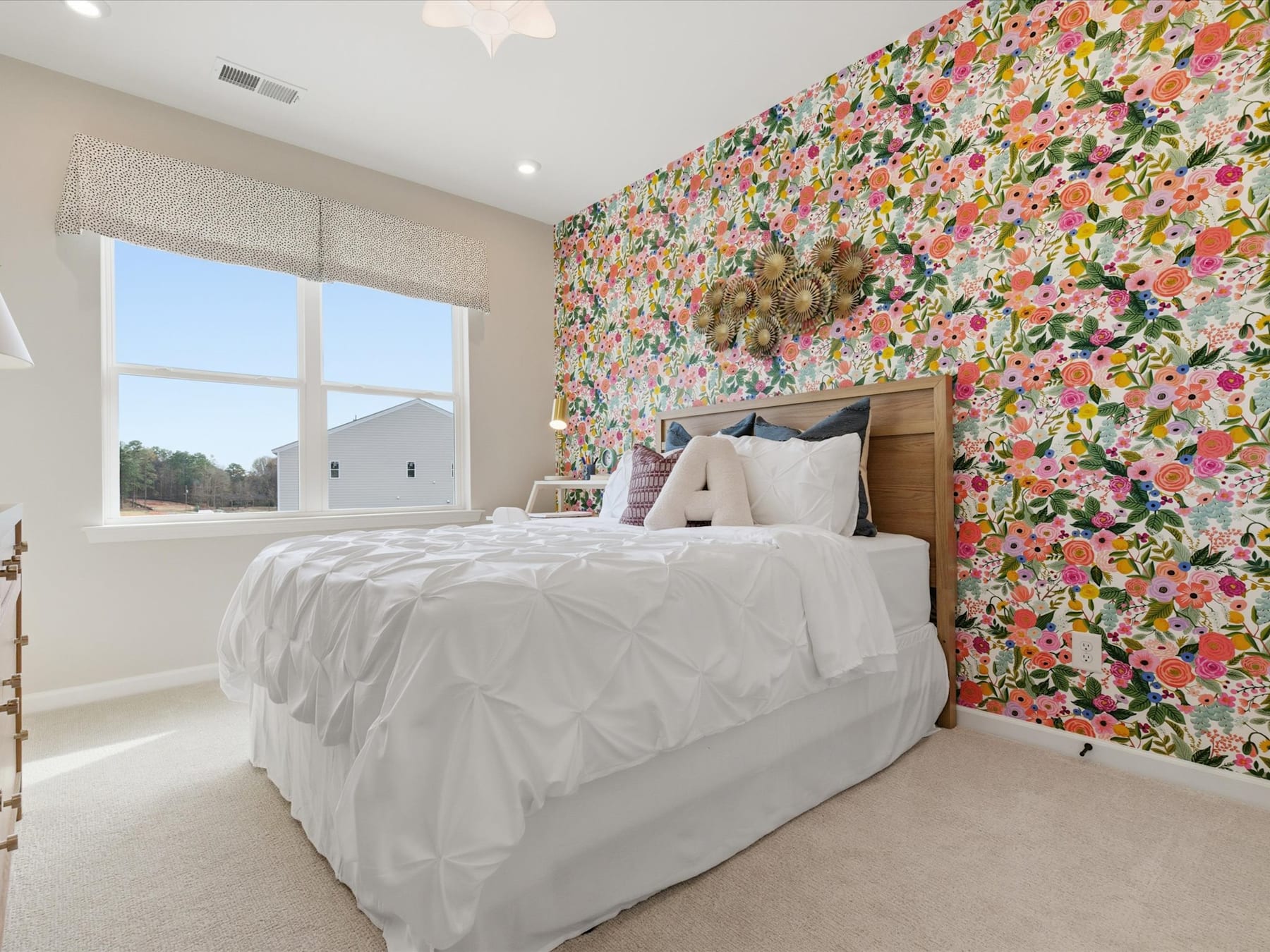 A bright and colorful floral wallpaper covers the walls of a cozy bedroom, complementing the white bedding and wooden furniture in the foreground.