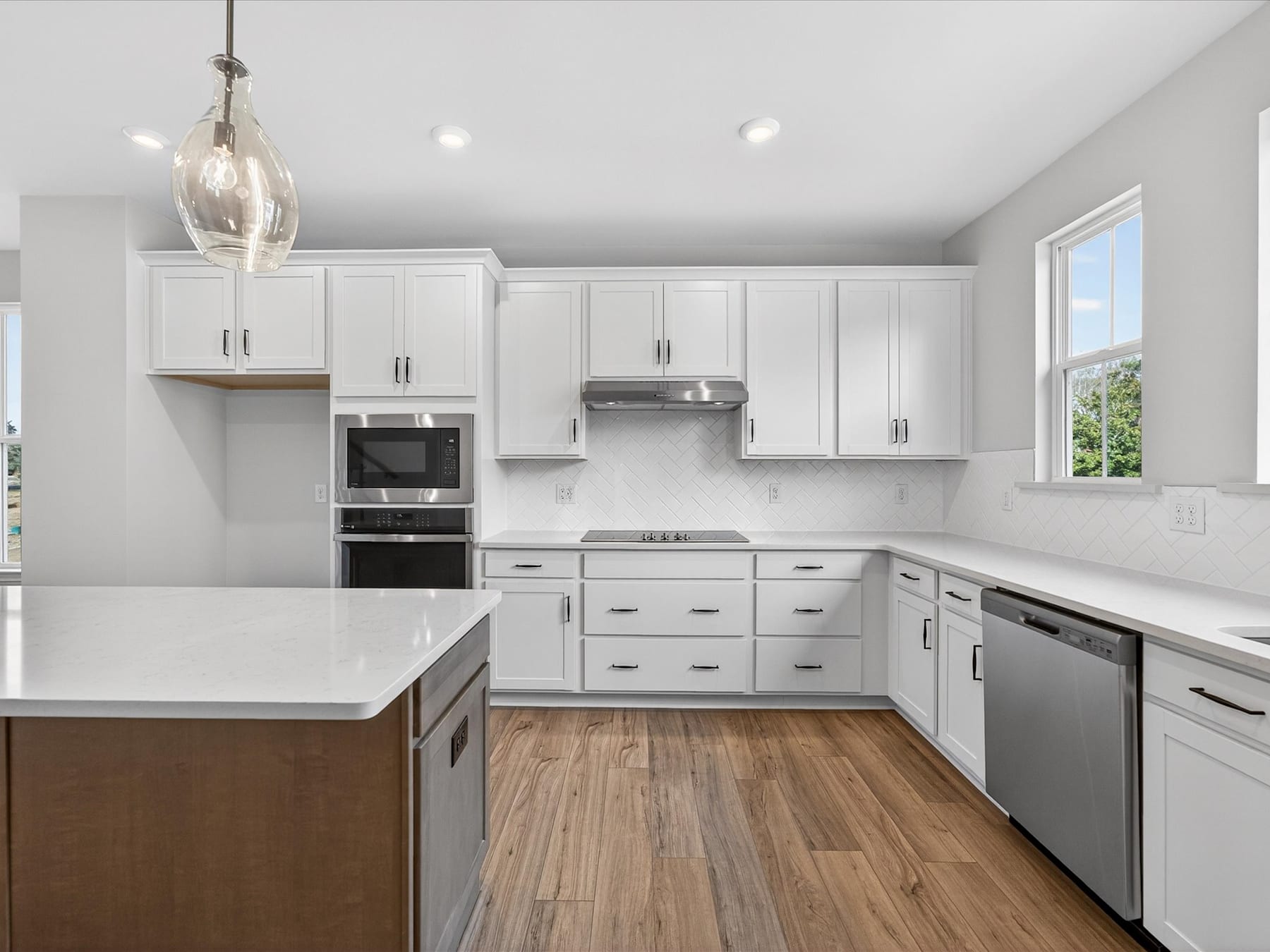 A modern, well-equipped kitchen with white cabinets, stainless steel appliances, and a wooden floor.