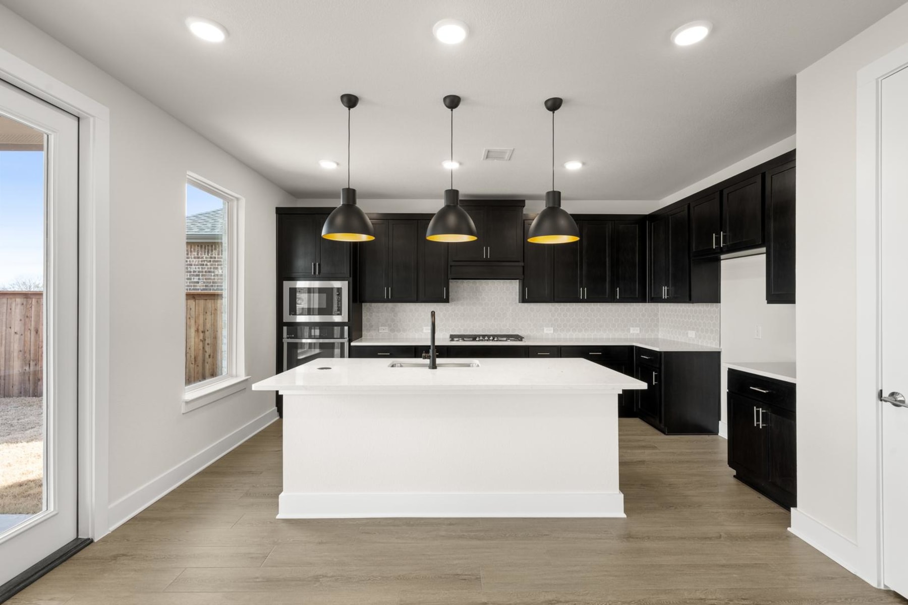 A modern, open-concept kitchen with dark cabinets, a white island, and pendant lighting fixtures creating a sleek and stylish atmosphere.