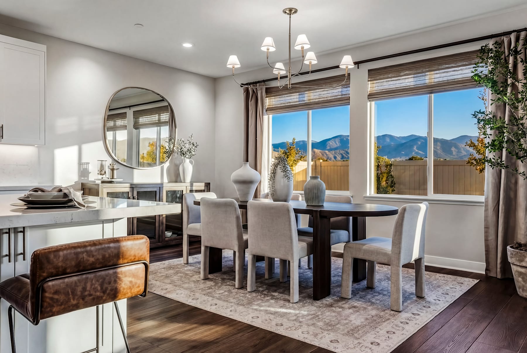 A modern and well-appointed dining room with a large window offering a scenic mountain view, featuring a wooden table, upholstered chairs, and decorative accents.
