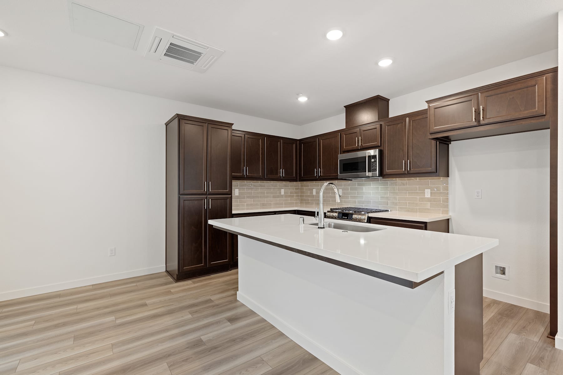 A modern kitchen with dark wood cabinets, a white countertop, and a tiled backsplash, set against a light-colored hardwood floor.
