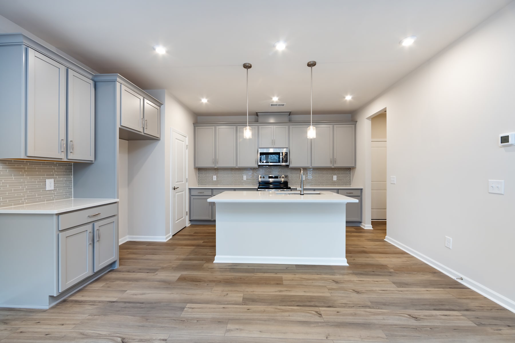 A modern, open-concept kitchen with white cabinets, a central island, and hardwood flooring, creating a bright and spacious atmosphere.