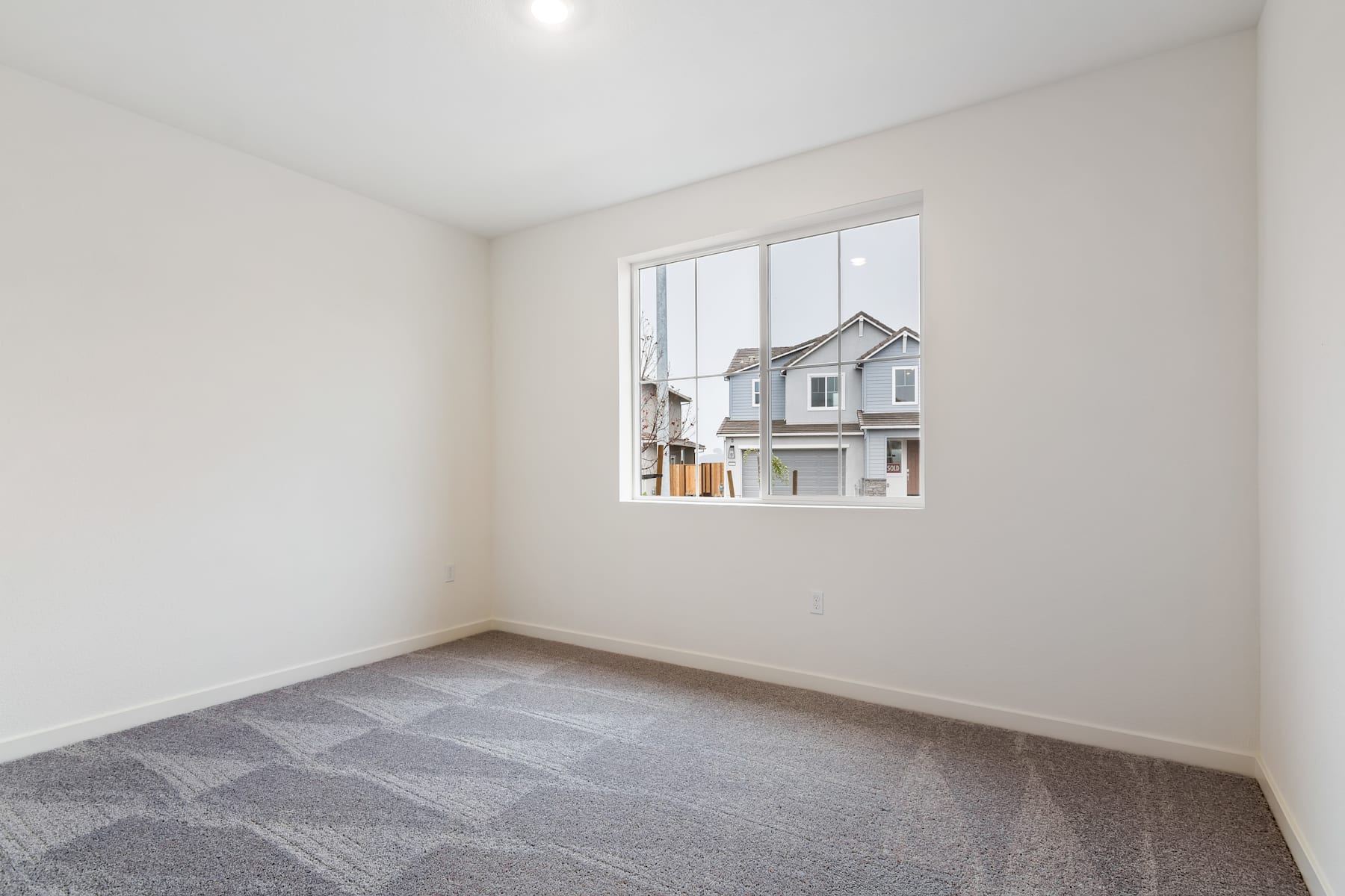 A sparsely furnished room with a large window overlooking a residential neighborhood in the background.