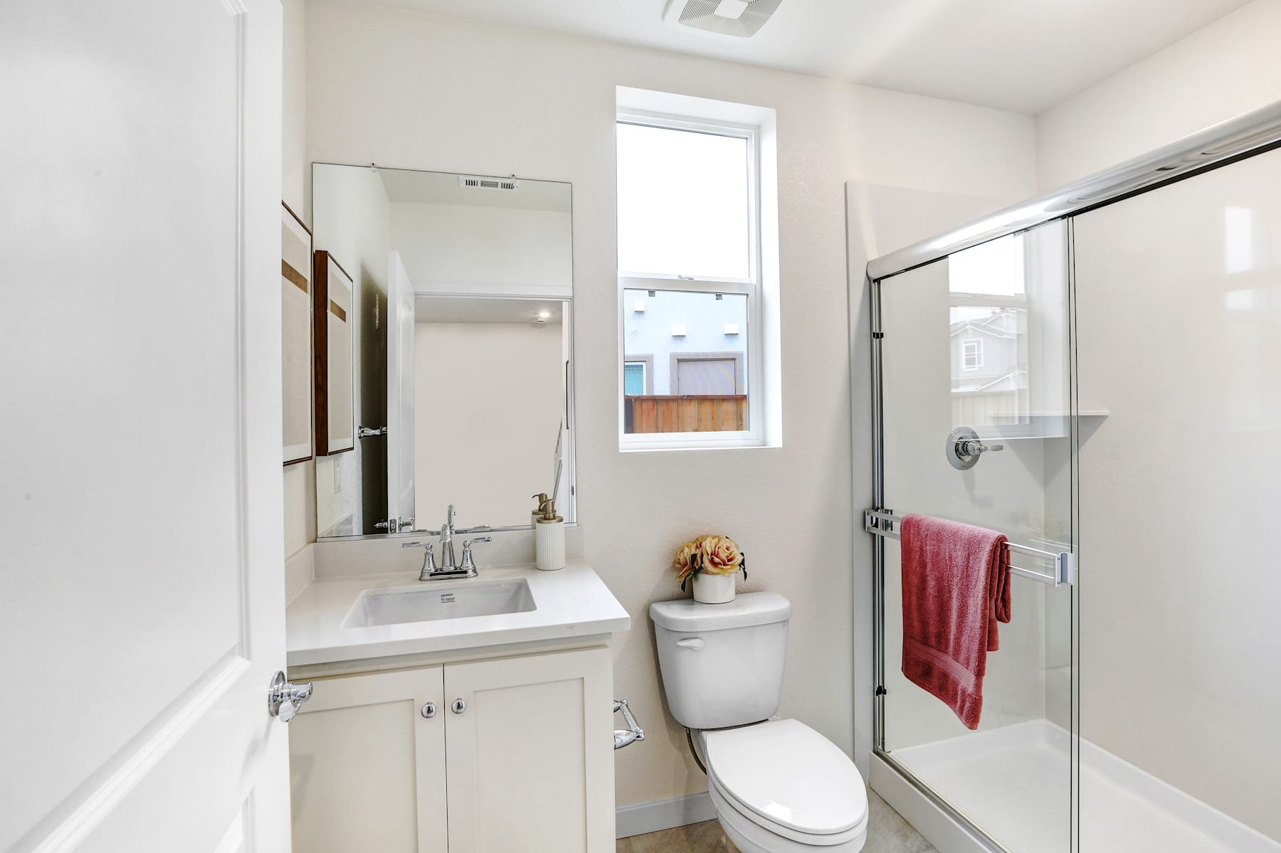 A bright and clean bathroom with a vanity, toilet, and glass-enclosed shower, featuring a small decorative item on the vanity.