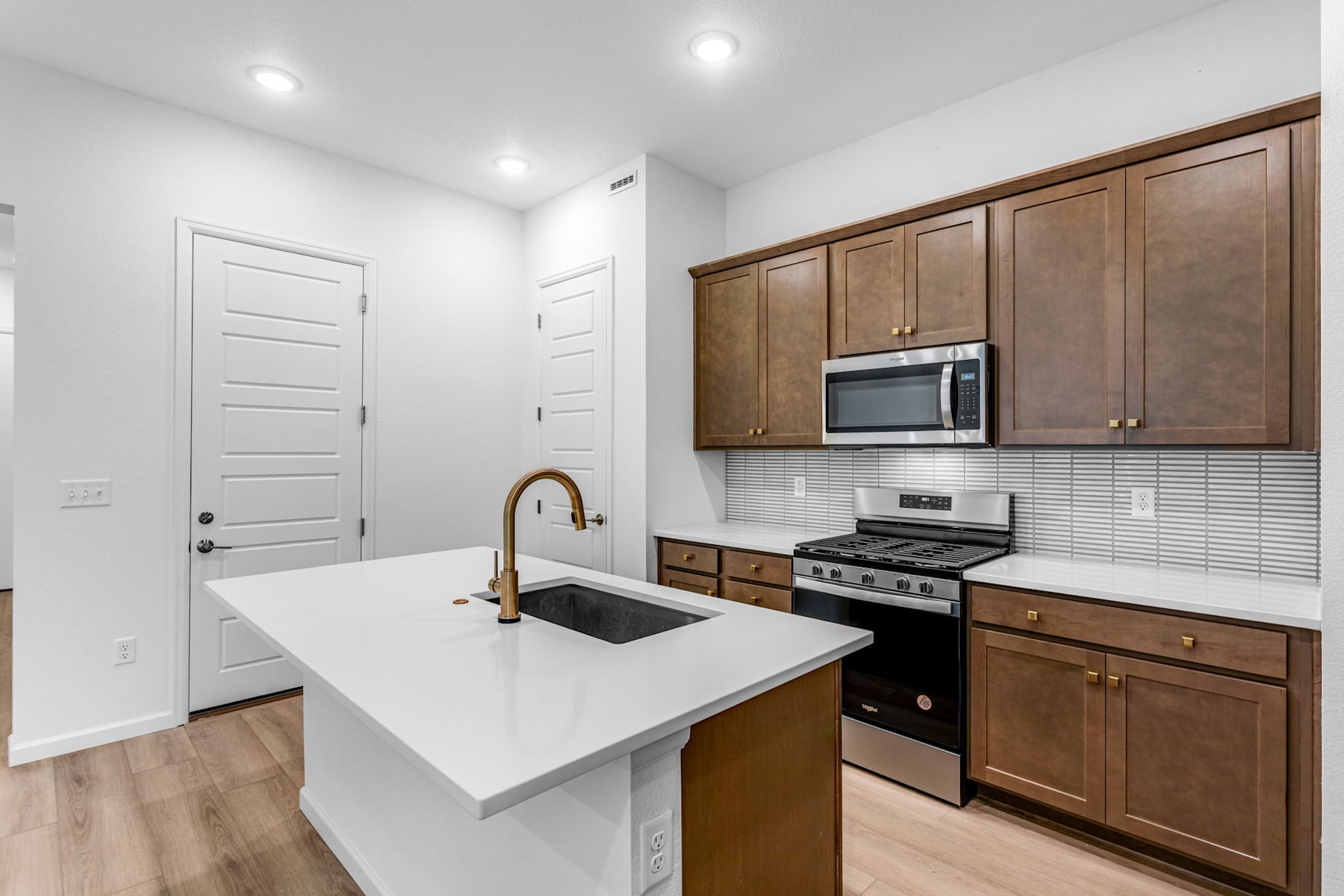 A modern kitchen with white countertops, wooden cabinets, and stainless steel appliances, including a microwave and oven, set against a bright and airy backdrop.