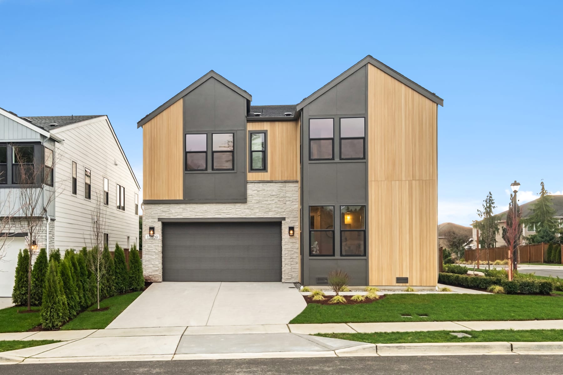 A modern two-story residential building with a garage, surrounded by a well-manicured lawn and landscaping, set against a clear blue sky.