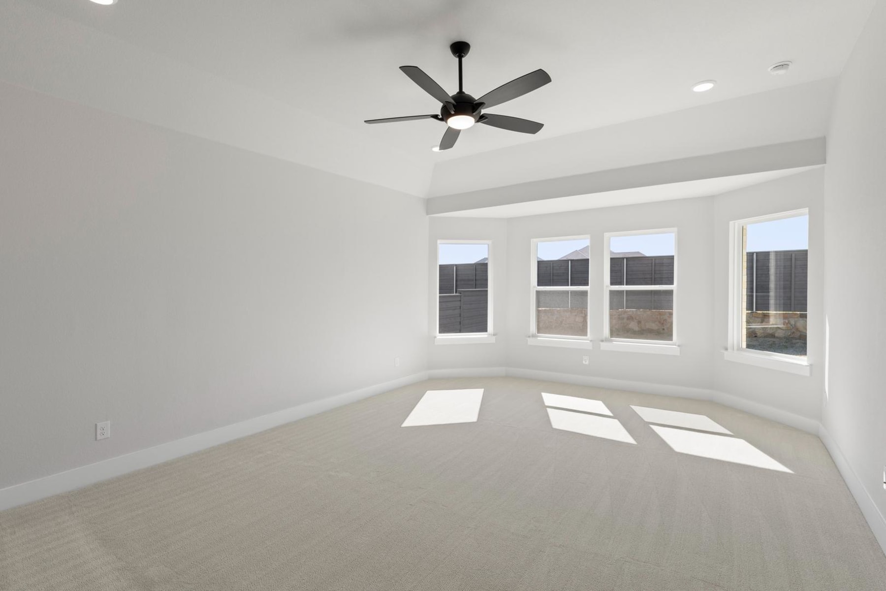 A spacious, well-lit room with a ceiling fan and large windows, providing a bright and airy atmosphere.