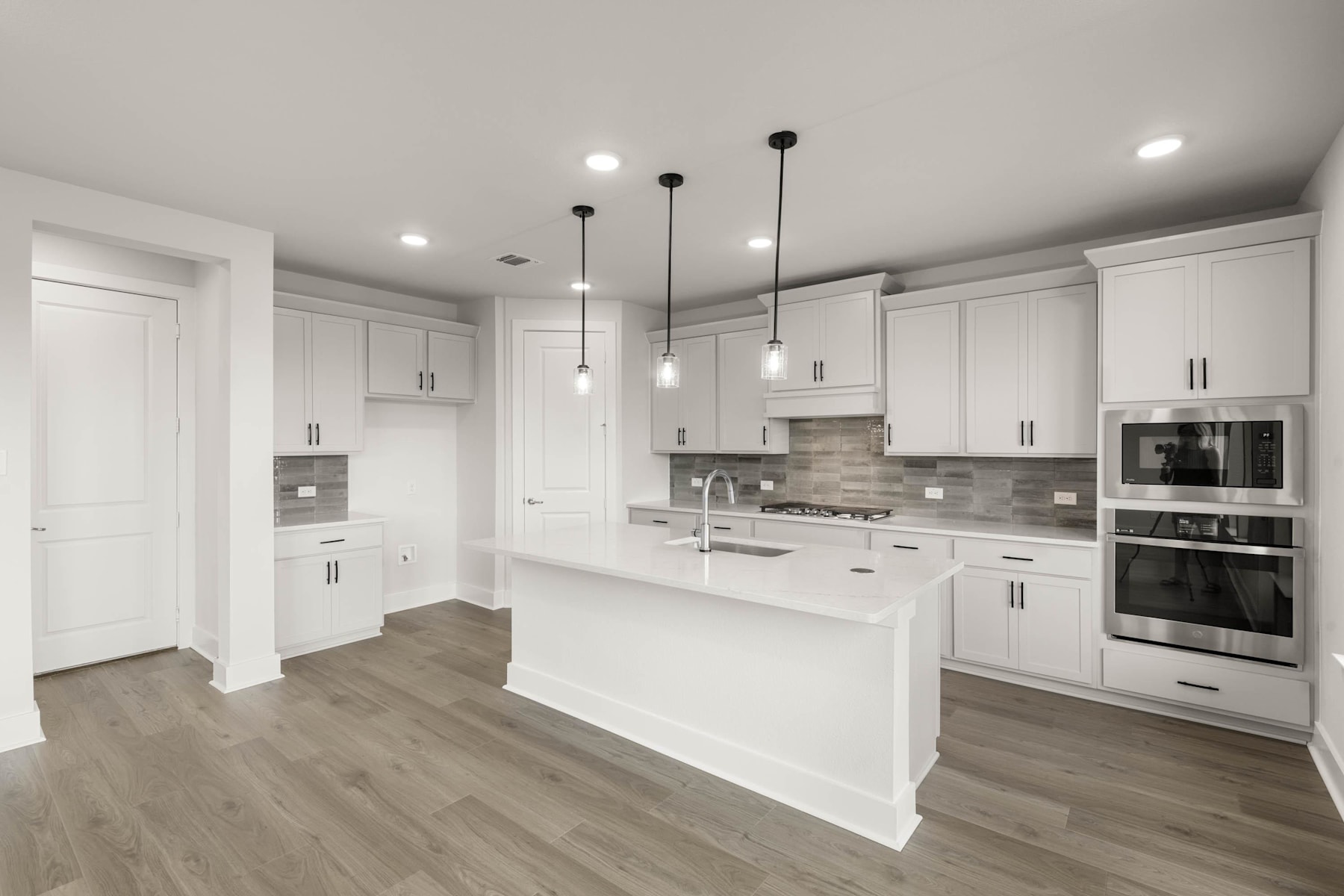 A modern, open-concept kitchen with white cabinets, gray countertops, and pendant lighting fixtures, set against a hardwood floor.
