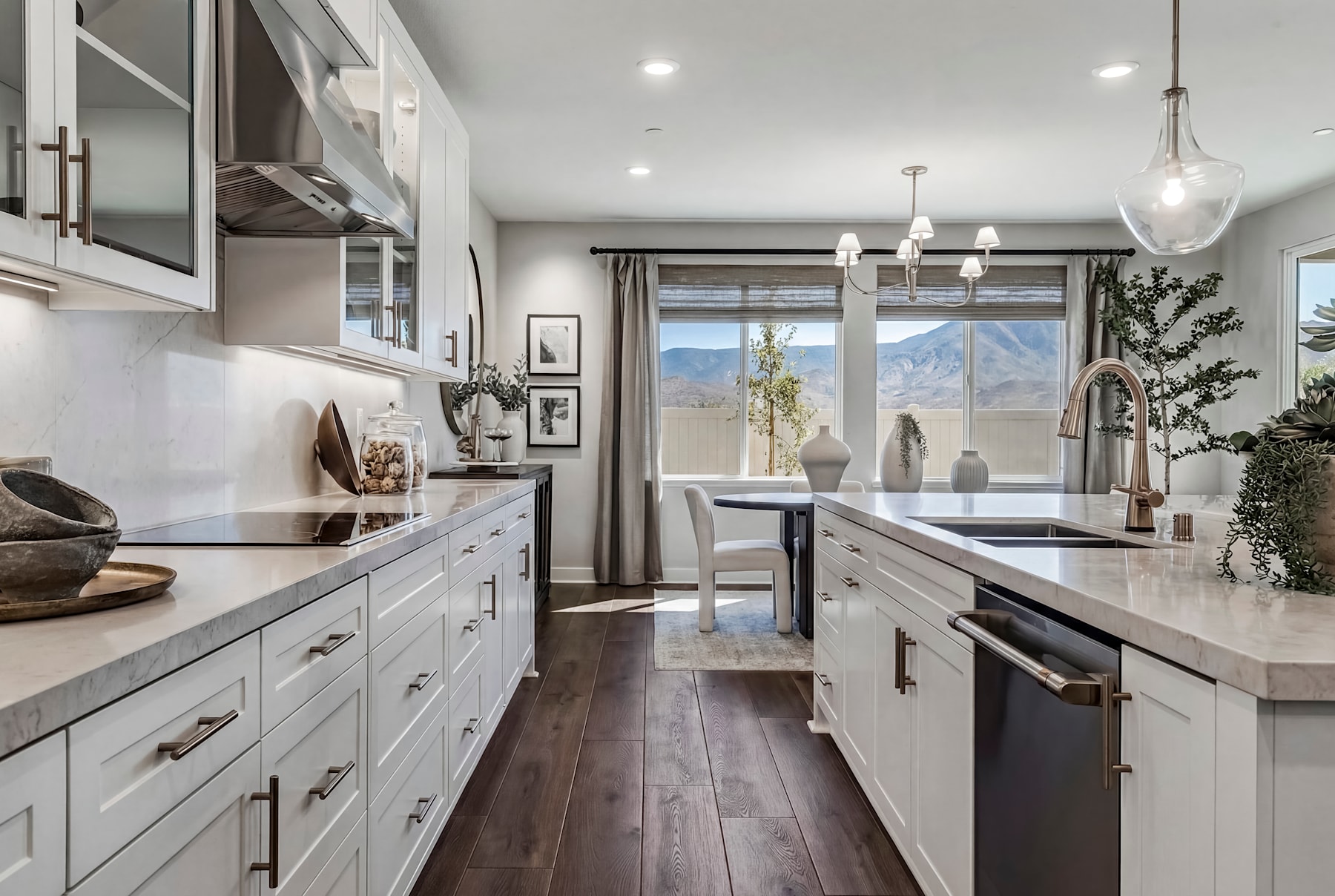 A modern, well-appointed kitchen with white cabinets, dark wood floors, and large windows offering a scenic mountain view in the background.