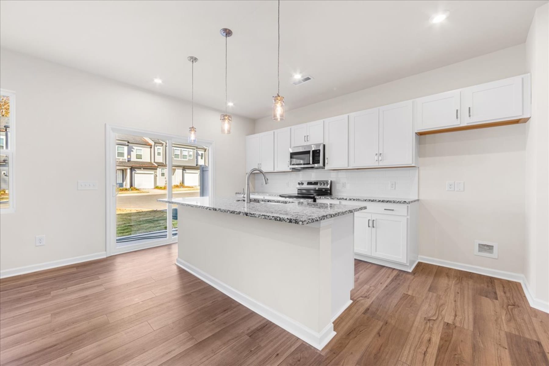 A modern, open-concept kitchen with white cabinets, granite countertops, and hardwood floors, leading to a bright and airy living space.
