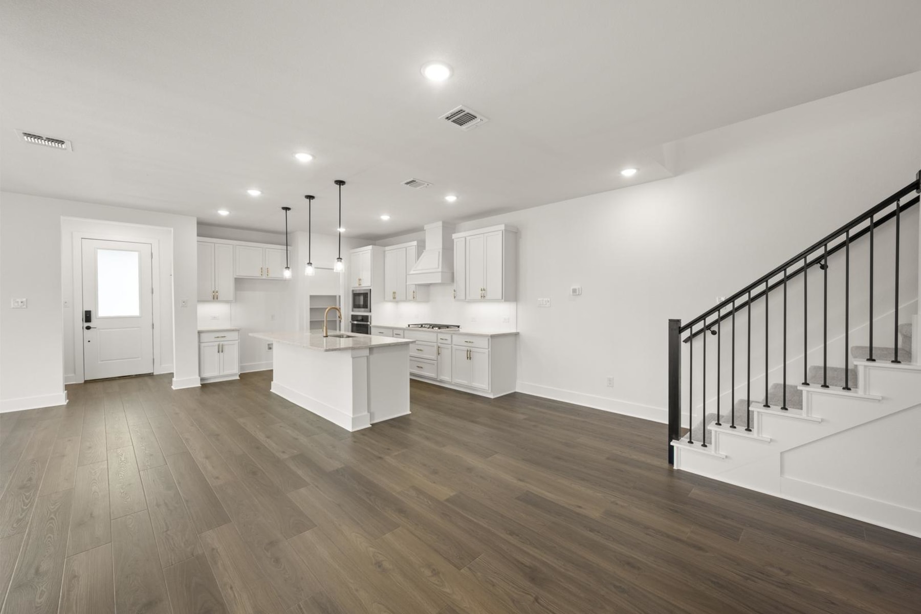 A modern, open-concept kitchen and living space with white cabinets, hardwood floors, and a staircase leading to an upper level.
