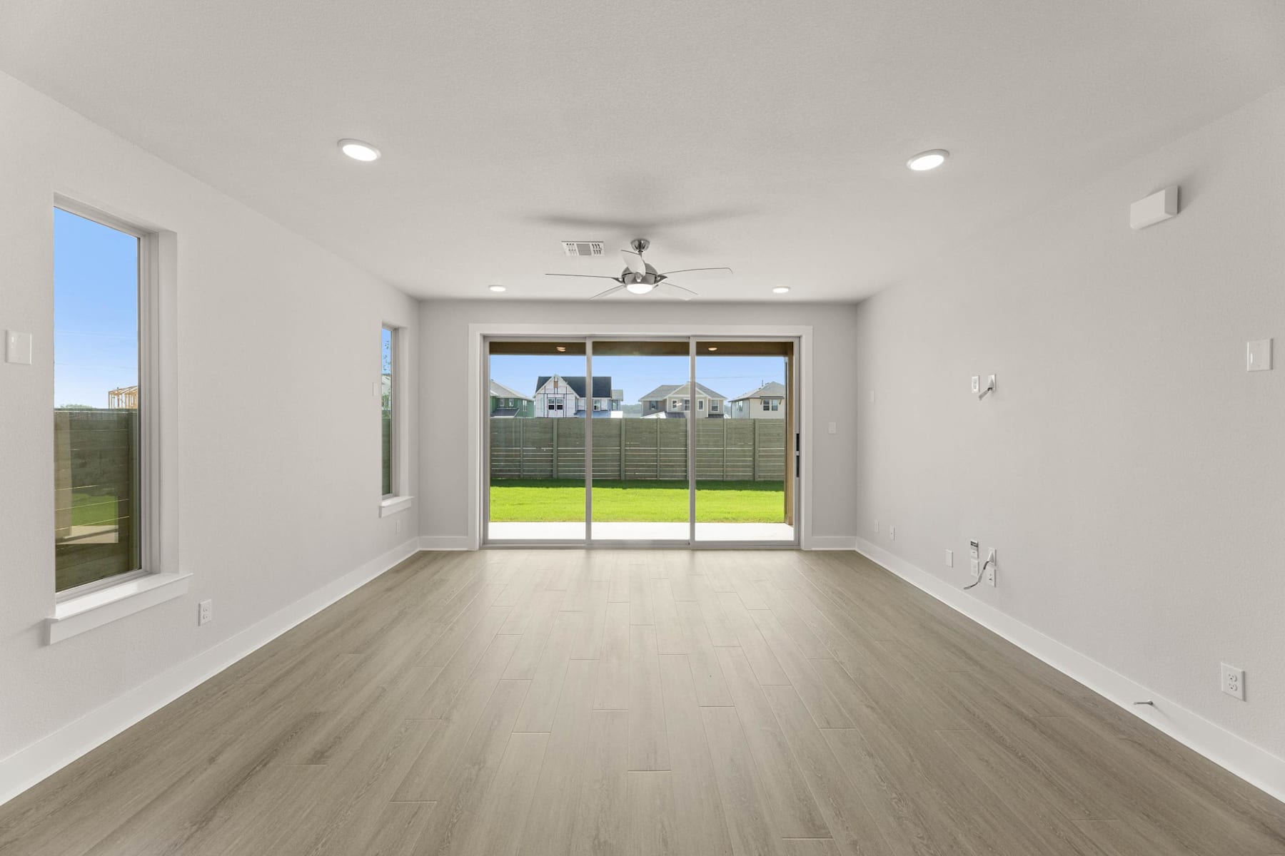 A spacious, bright room with a sliding glass door leading to a grassy backyard, featuring hardwood floors and recessed lighting.