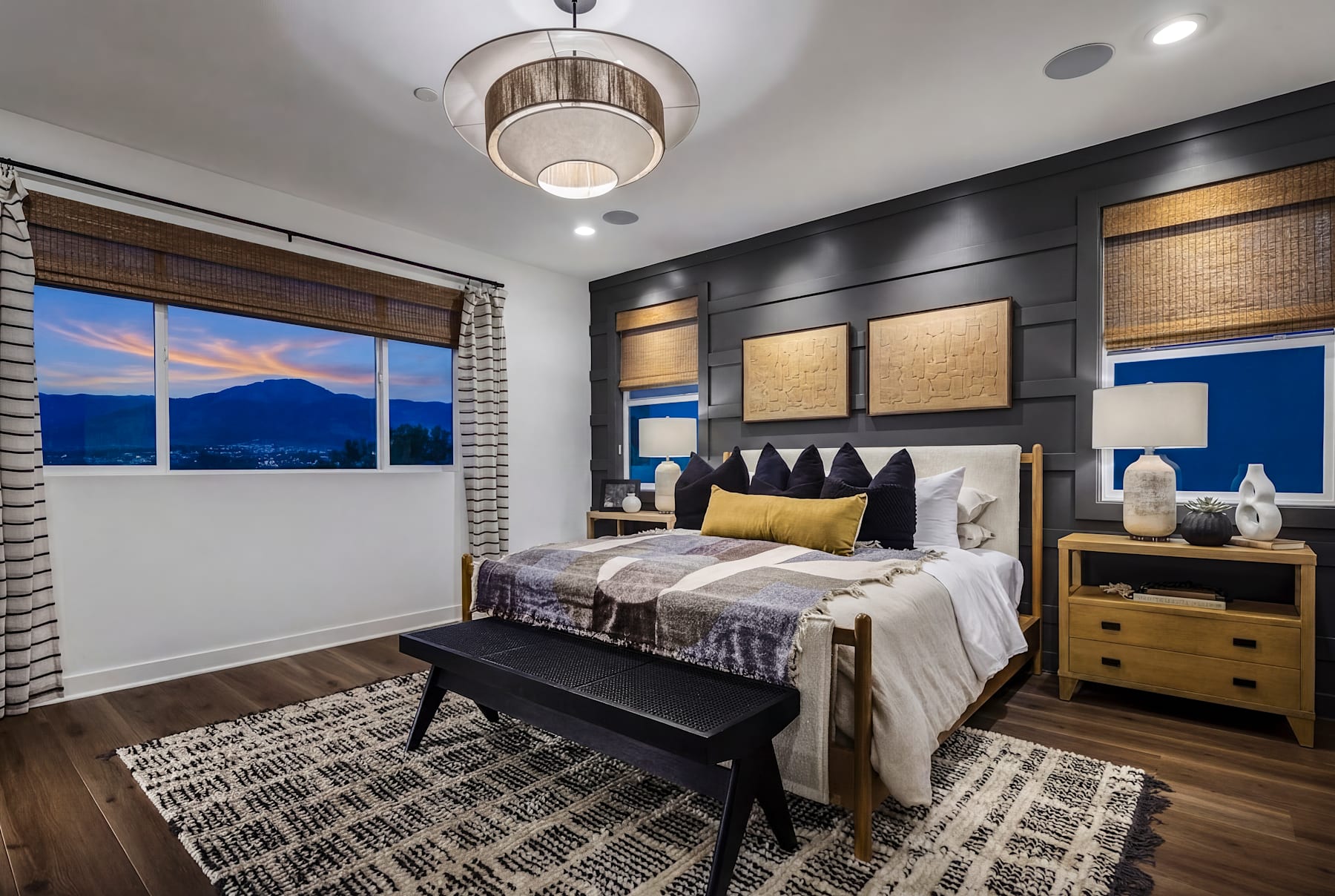 A cozy and modern bedroom with a large window overlooking a scenic mountain landscape, featuring a plush bed, wooden furniture, and decorative accents.