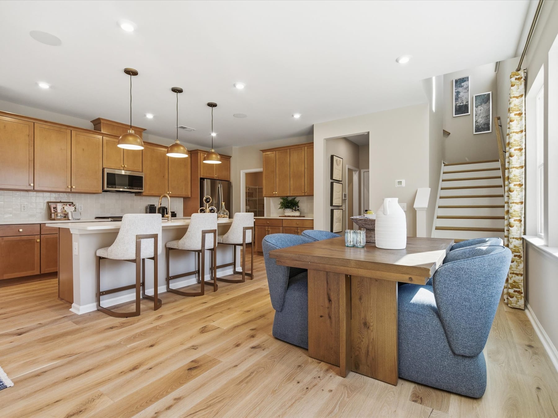 A modern and open-concept kitchen and living room with wooden cabinets, a large wooden dining table, and a comfortable blue sofa in the foreground.