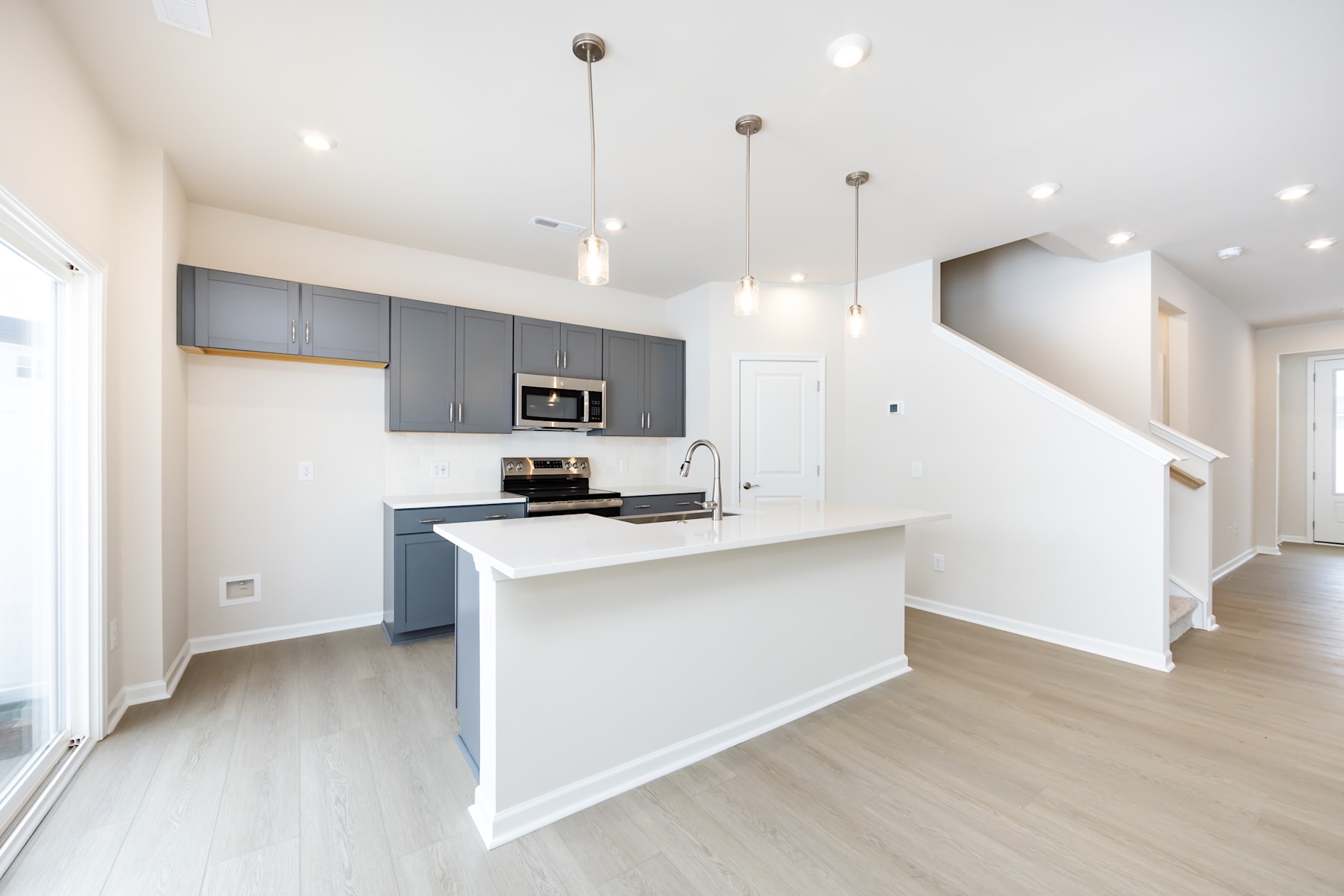 A modern, open-concept kitchen with gray cabinets, white countertops, and pendant lighting, leading into a bright and airy living space with hardwood floors.