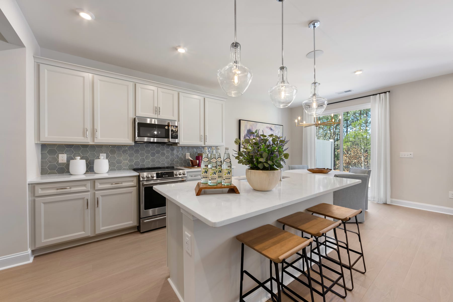 A modern, bright kitchen with white cabinets, a large island with stools, and pendant lighting fixtures hanging above.