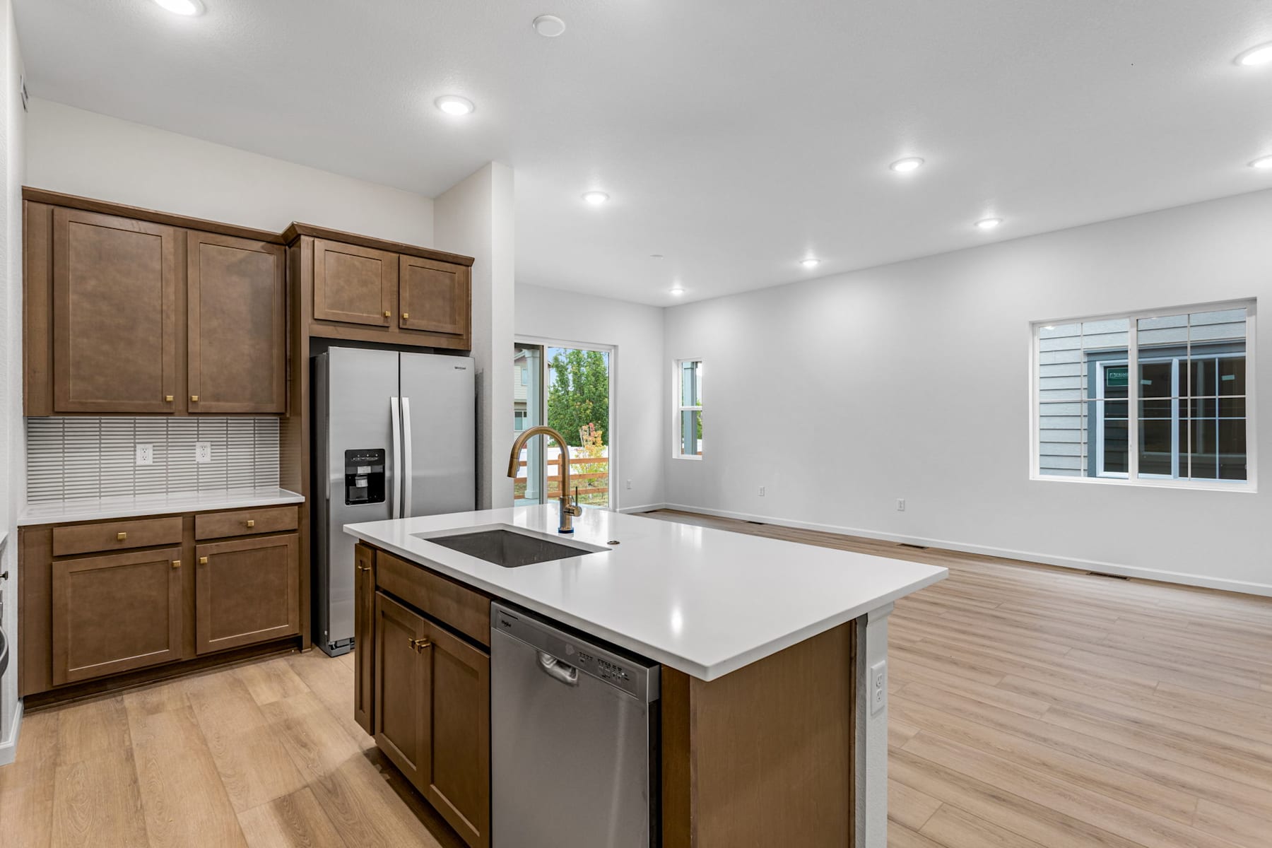 A modern, well-lit kitchen with wooden cabinets, a stainless steel refrigerator, and a central island with a white countertop.