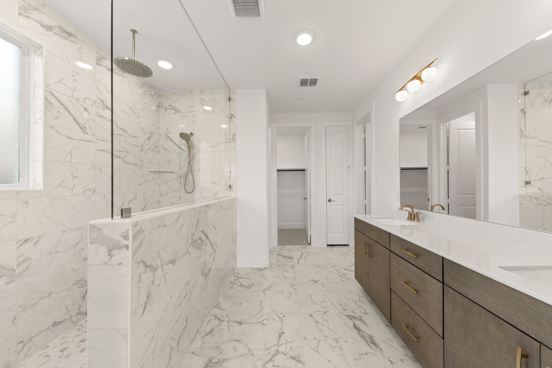A spacious and modern bathroom with a large vanity, a glass-enclosed shower, and a marble-tiled floor and walls, creating a sleek and elegant atmosphere.