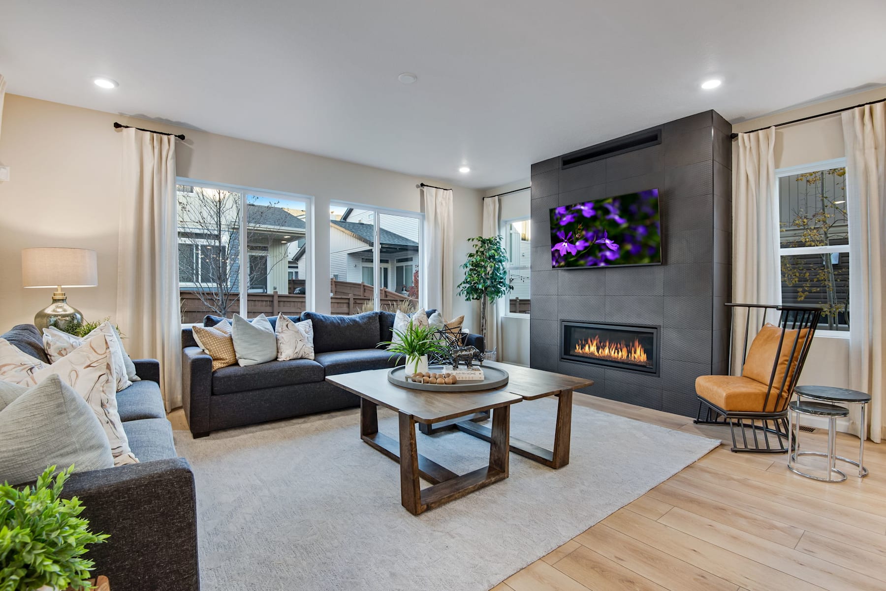 A cozy and modern living room with a fireplace, comfortable seating, and a vibrant artwork on the wall, surrounded by large windows that let in natural light.