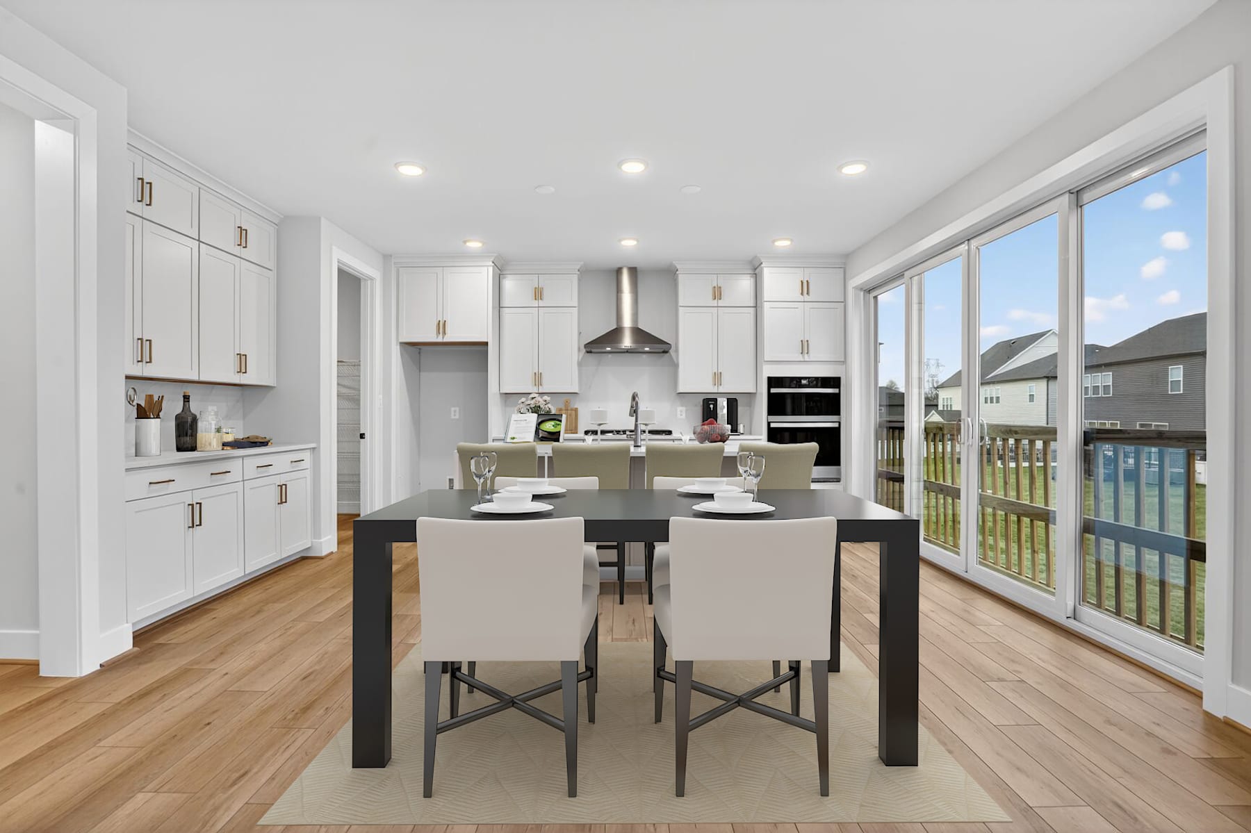 A modern, bright, and spacious kitchen with white cabinets, a large window overlooking a scenic outdoor area, and a dining table with chairs in the foreground.