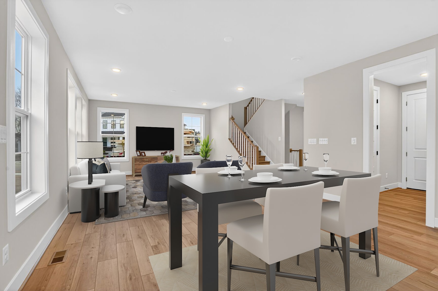 A modern and minimalist open-concept living and dining area with a large window, hardwood floors, and a mix of dark and light furniture.