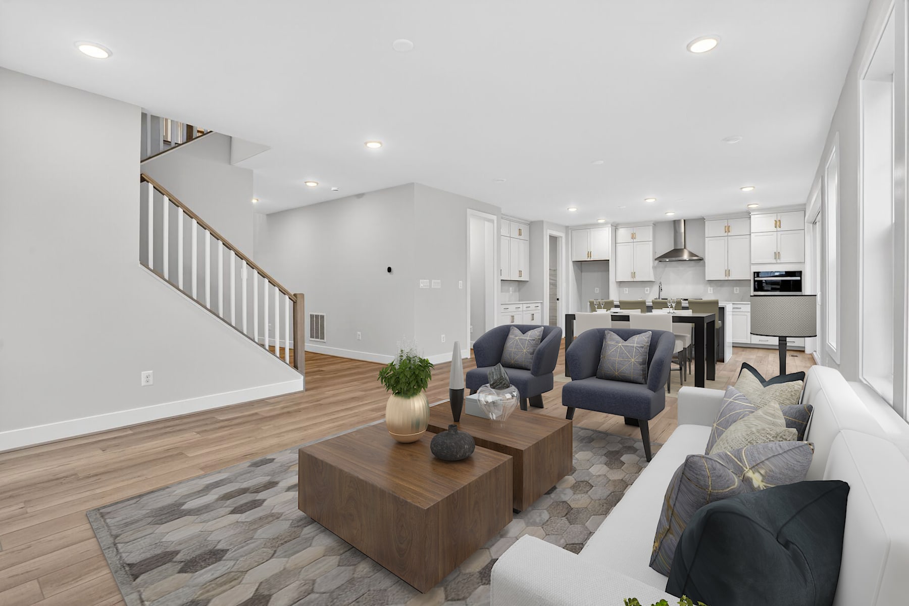 A modern and spacious open-concept living area with a kitchen, dining, and living room, featuring a wooden coffee table, gray sofas, and a staircase leading to the upper level.